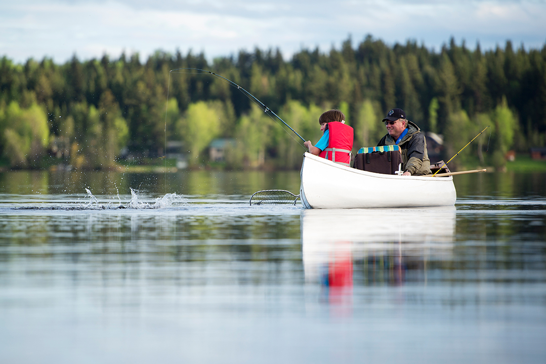 Father and son fishing in a canoe with a fish on the line